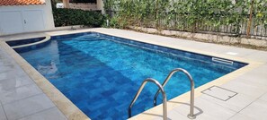 A rectangular swimming pool with a metal ladder, surrounded by a tiled deck.