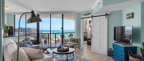 A spacious living room with a large window overlooking the beach, a sofa, a coffee table, and a television.