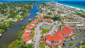 An aerial view of a coastal residential area with a marina, houses with red roofs, and a large building with a tennis court. - St Thomas Square Villa 1211c Beach Bumz (Panama City Beach)