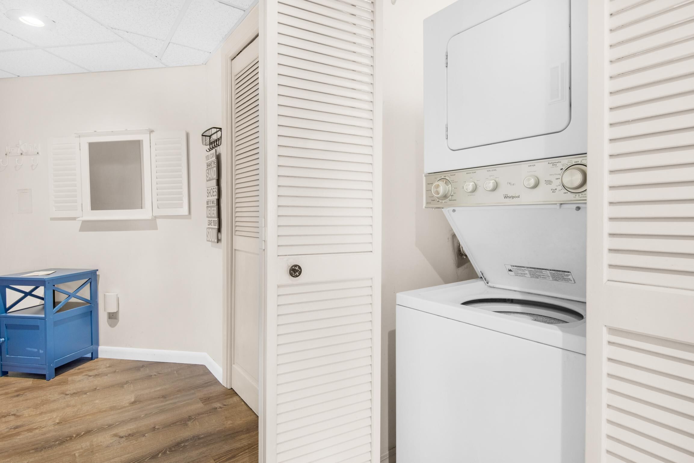 A laundry room with a stacked washer and dryer, a blue storage bin, and a white door with a window.