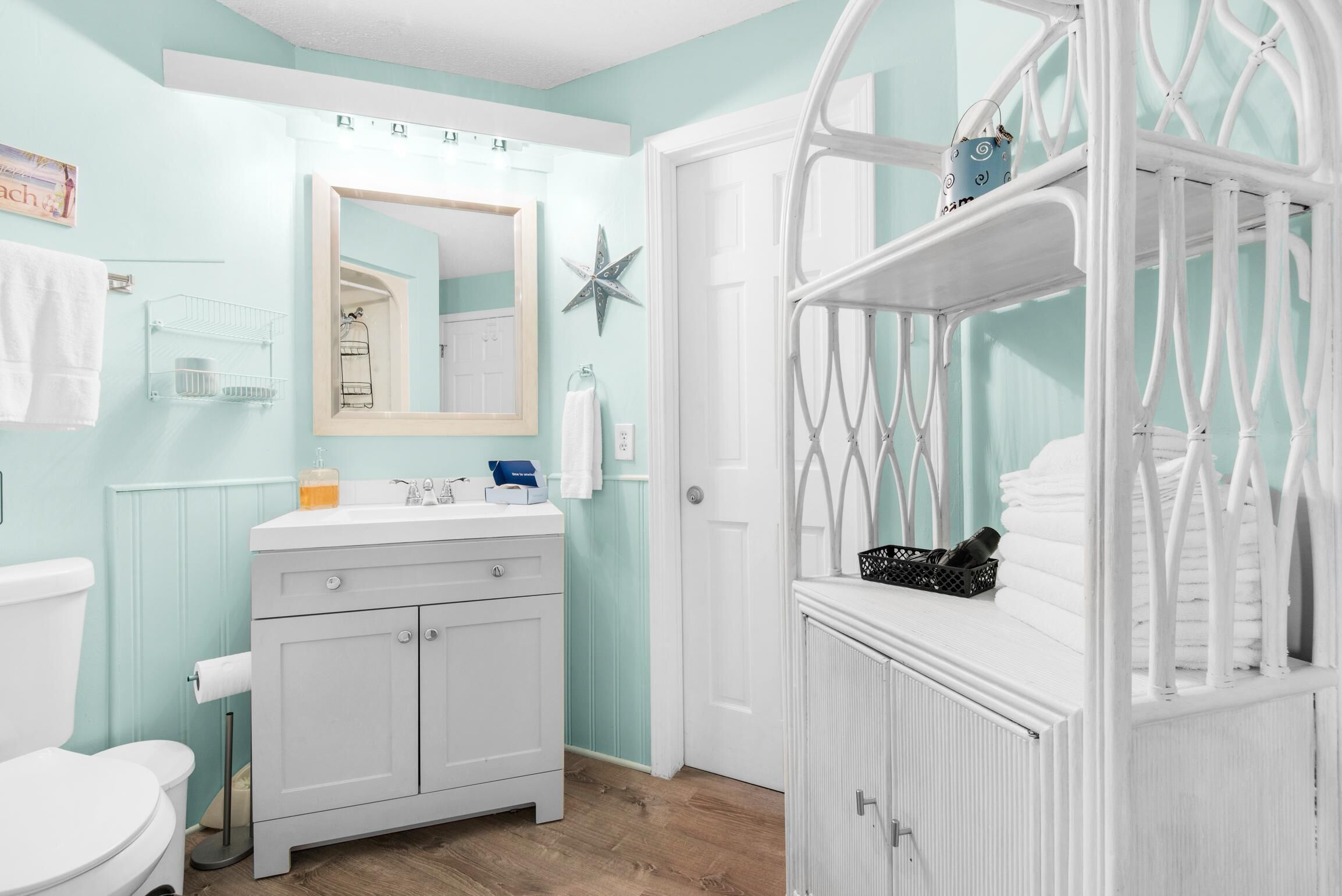 Une salle de bain avec un meuble-lavabo blanc, un miroir, une décoration en forme d’étoile et une porte blanche.