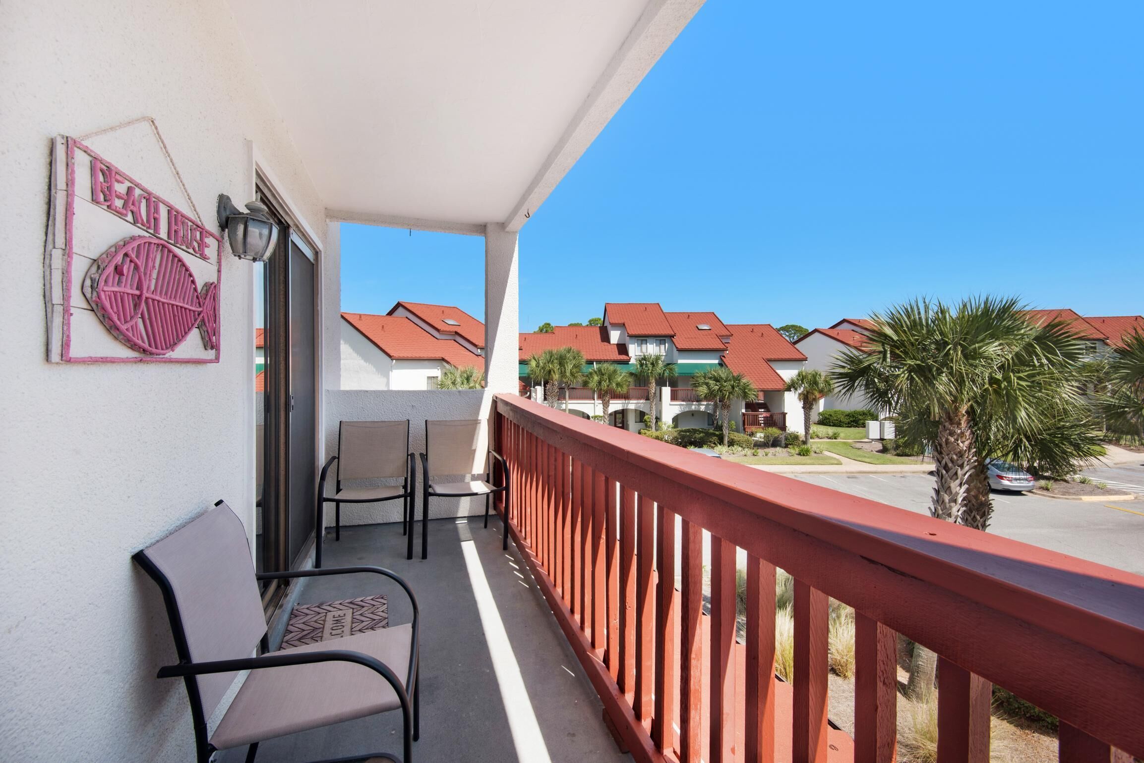 Een balkon met stoelen, een rode reling en een bord waarop staat 'Beach House'.