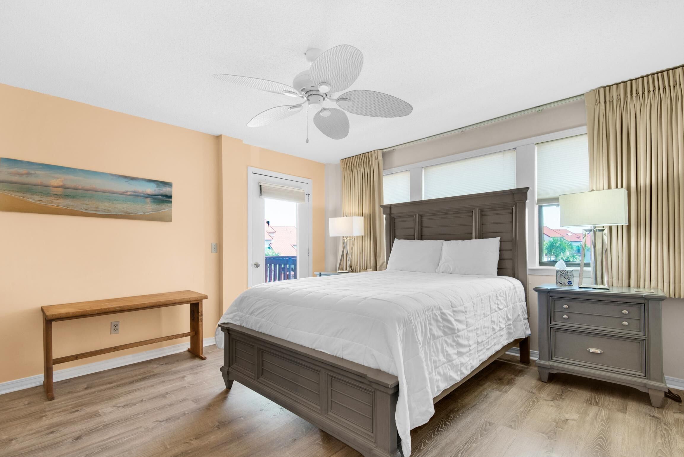 A bedroom with a bed, a nightstand, a bench, a ceiling fan, and a painting on the wall.