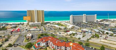 An aerial view of a coastal area with a hotel, a large parking lot, and a beach access sign.