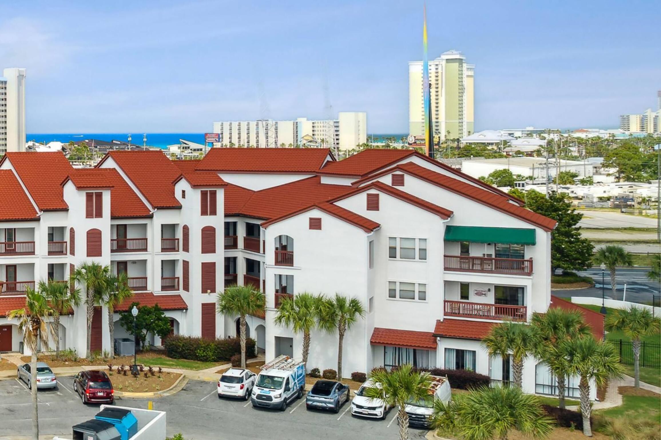 Un hôtel à plusieurs étages, avec des toits recouverts de tuiles rouges, des balcons et un parking où sont garées plusieurs voitures.