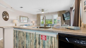 A kitchen with a built-in dishwasher, a ceiling fan, and a fire extinguisher sign. - St Thomas Square Villa 1211c Beach Bumz (Panama City Beach)