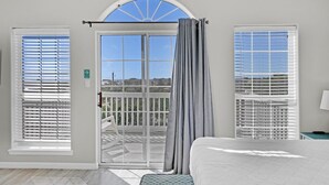 A bedroom with a large bed, a balcony with a view, and two windows with blinds. - Bluebonnet by the Beach (Santa Rosa Beach)