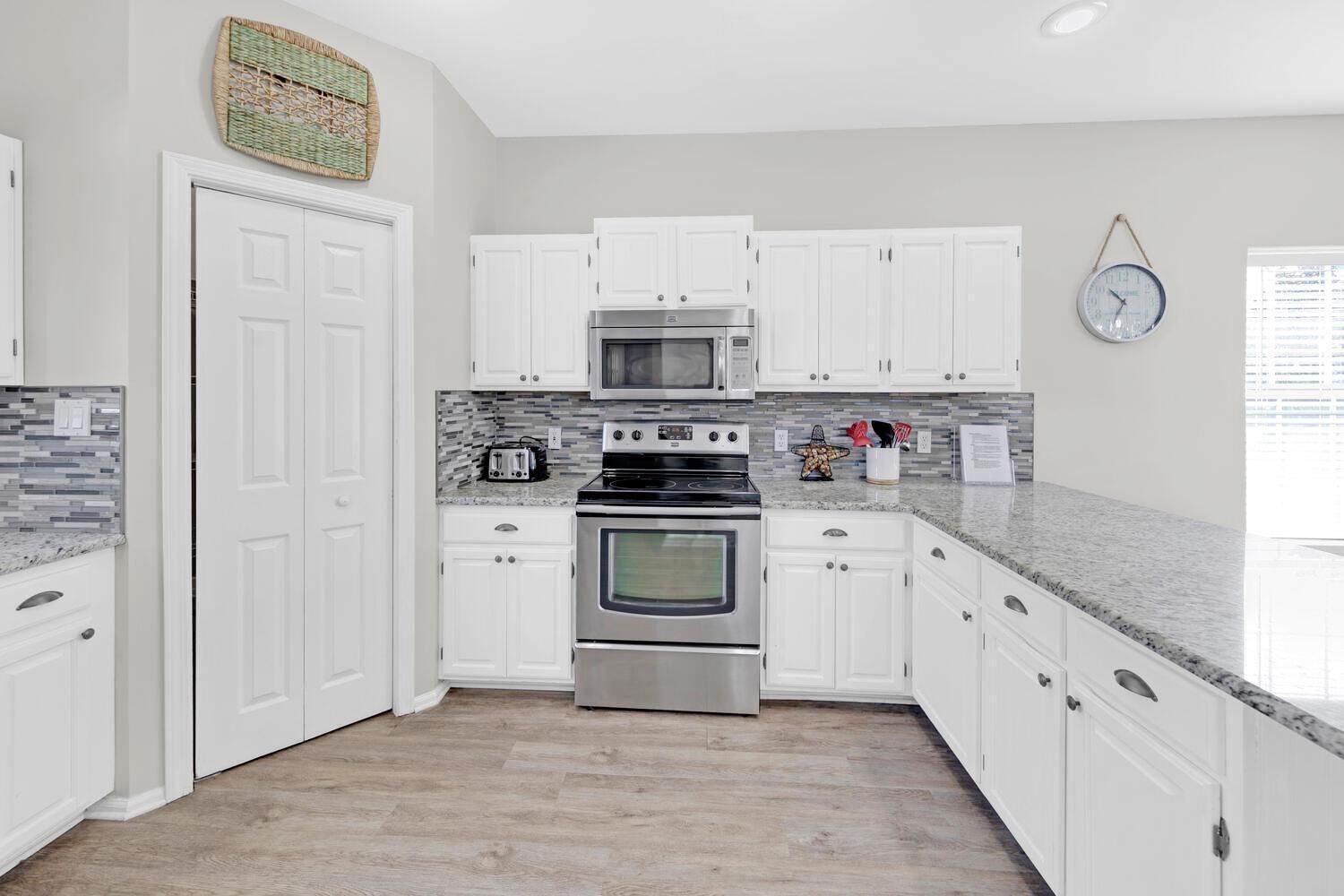 A modern kitchen with white cabinets, stainless steel appliances, and a tiled backsplash.