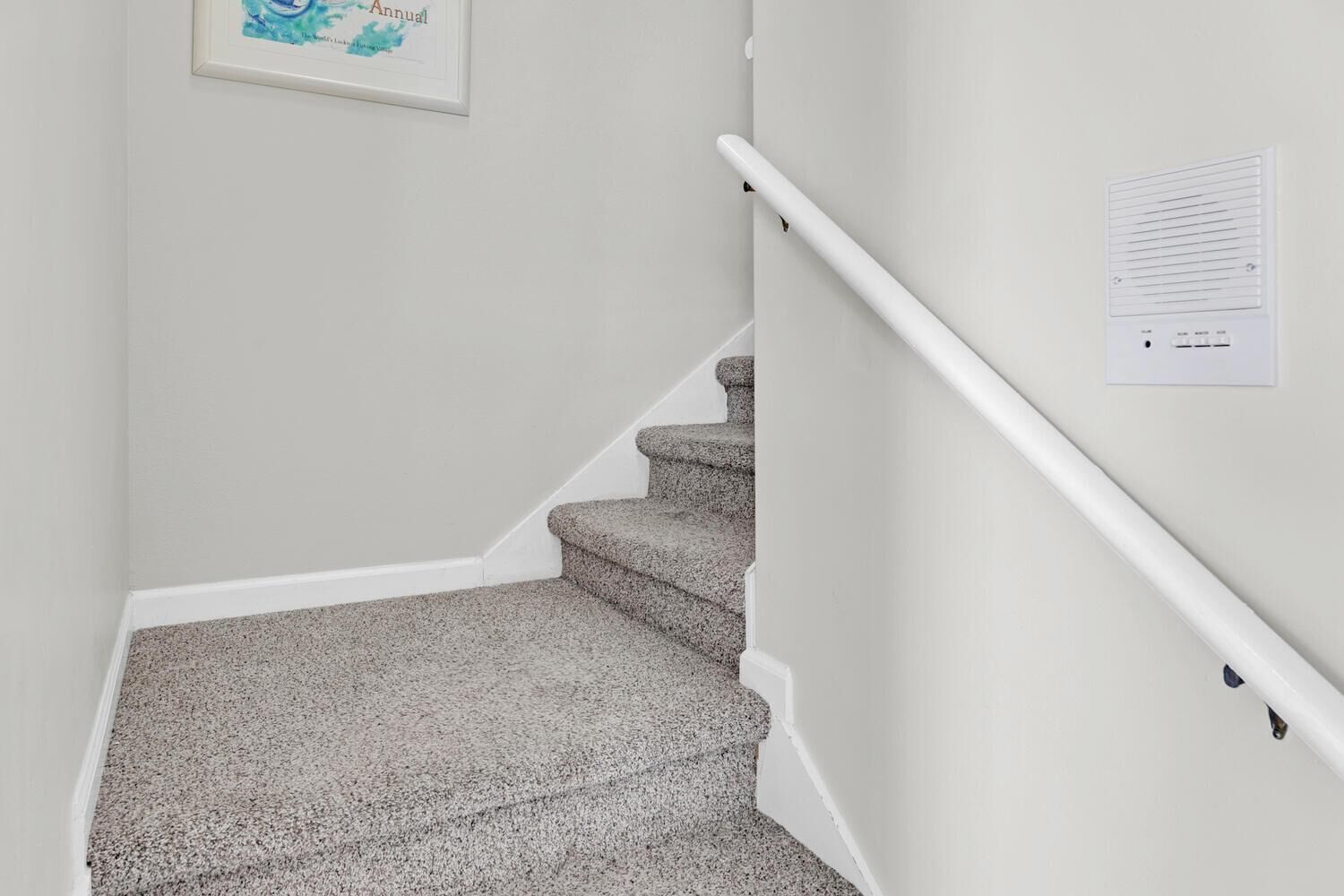 A staircase with carpeted steps and a handrail, leading to a landing with a framed map.