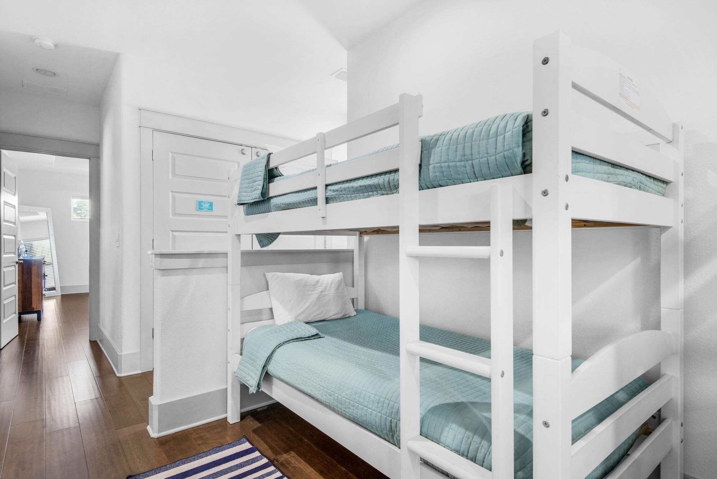 A bunk bed room with white walls, a wooden floor, and a door with a sign.