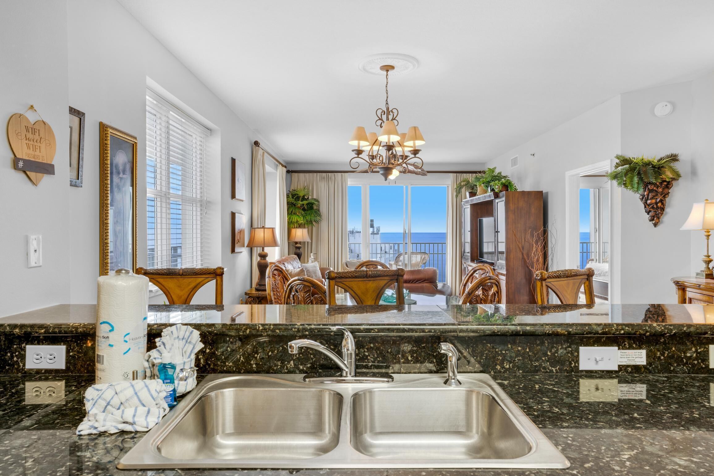 A modern kitchen with a double sink, granite countertops, and a view of the ocean through large windows.