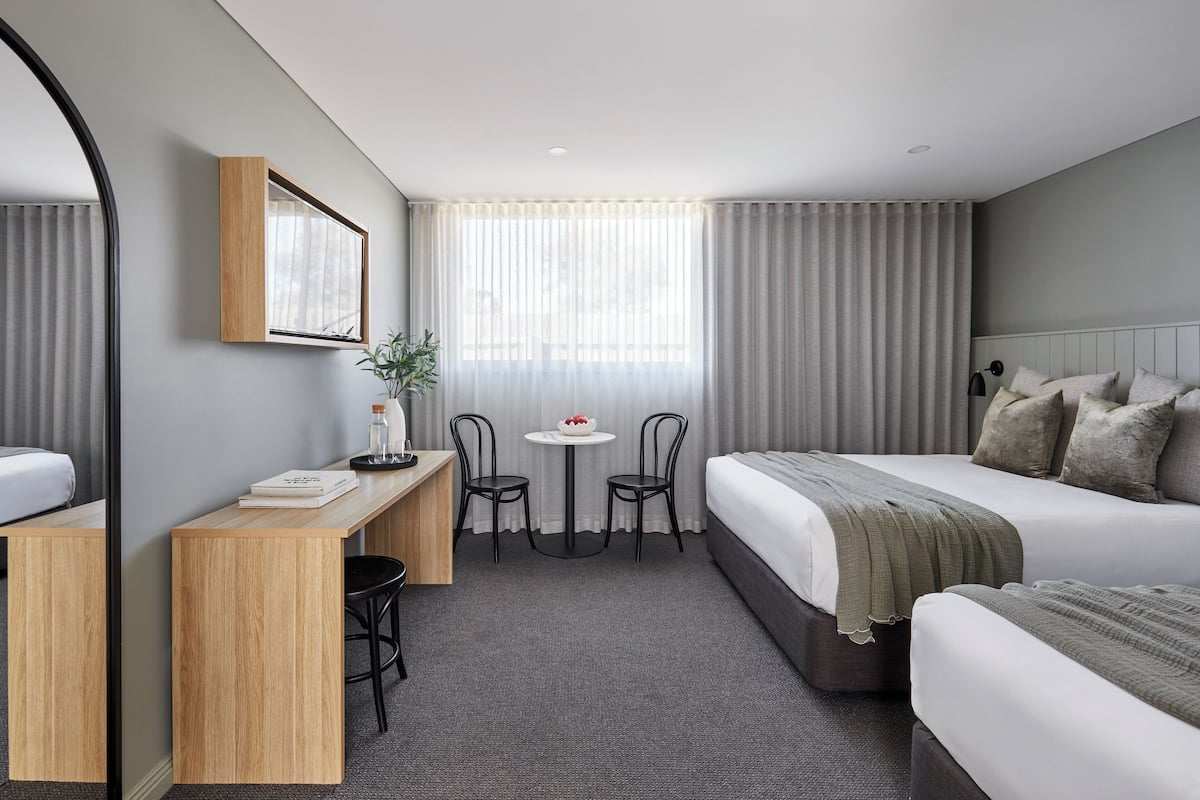 A hotel room with a bed, a desk, two chairs, a small table, and a large window with curtains.
