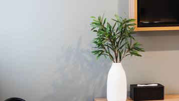 A modern room with a round table, two chairs, a white vase with a plant, a black box, and a mounted television.
