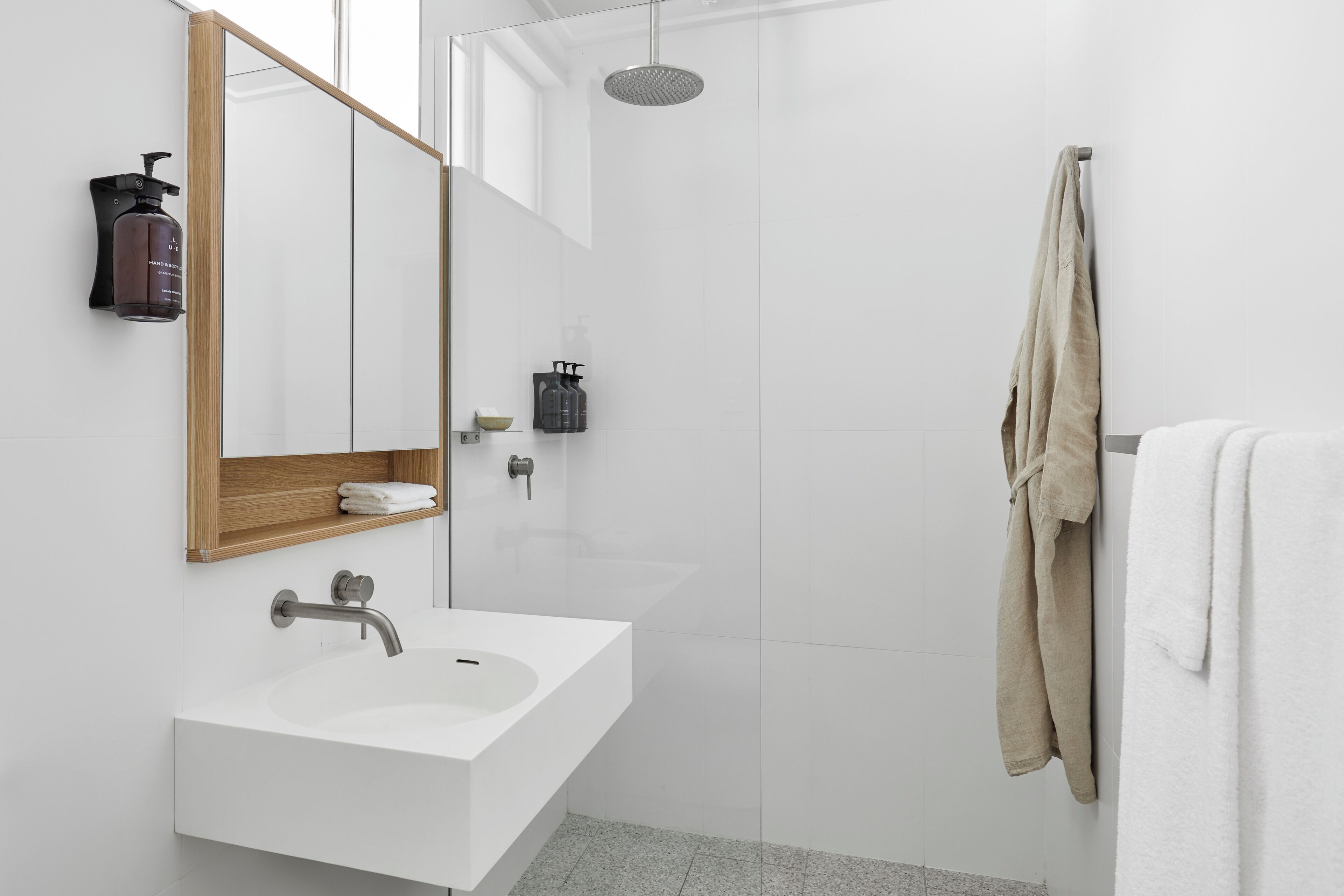 Une salle de bain moderne avec un lavabo blanc, un miroir, une douche et un porte-serviettes.