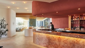 Un área de bar moderna con mostrador de mármol, un barman y una estantería con botellas de vino.