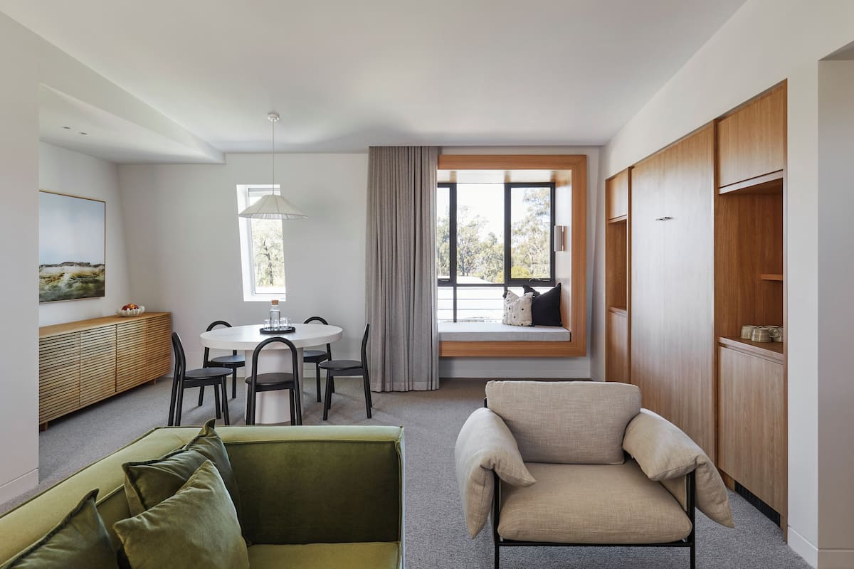 A modern living room with a sofa, armchair, dining table, and built-in wooden cabinets.