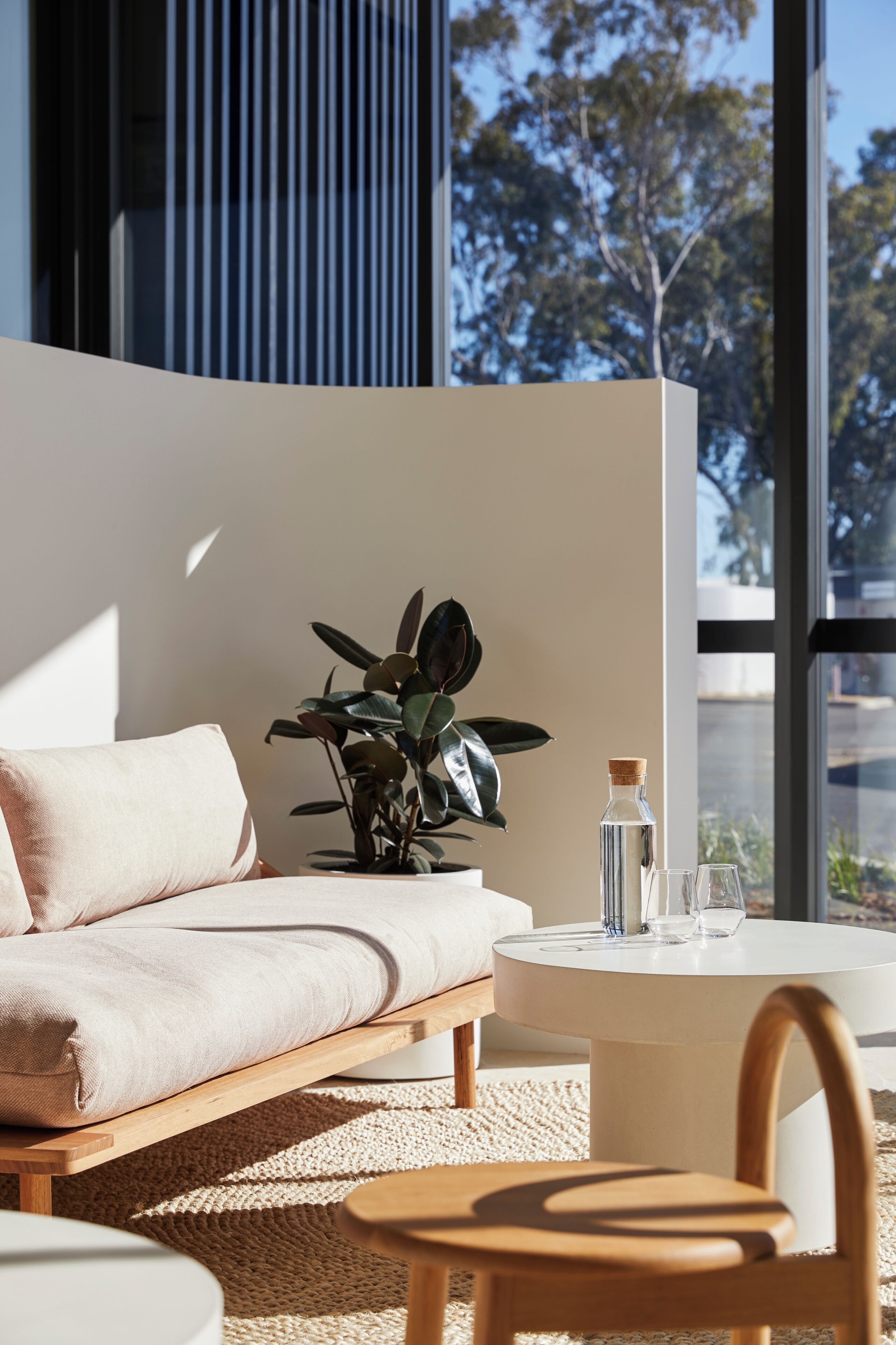 Ein modernes Wohnzimmer mit einer Couch, einem Couchtisch und einem Sessel. Auf dem Tisch steht eine Pflanze und das Fenster bietet Blick auf Bäume.