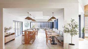 Un comedor amplio con largas mesas y sillas de madera, ventanas grandes y lámparas colgantes.