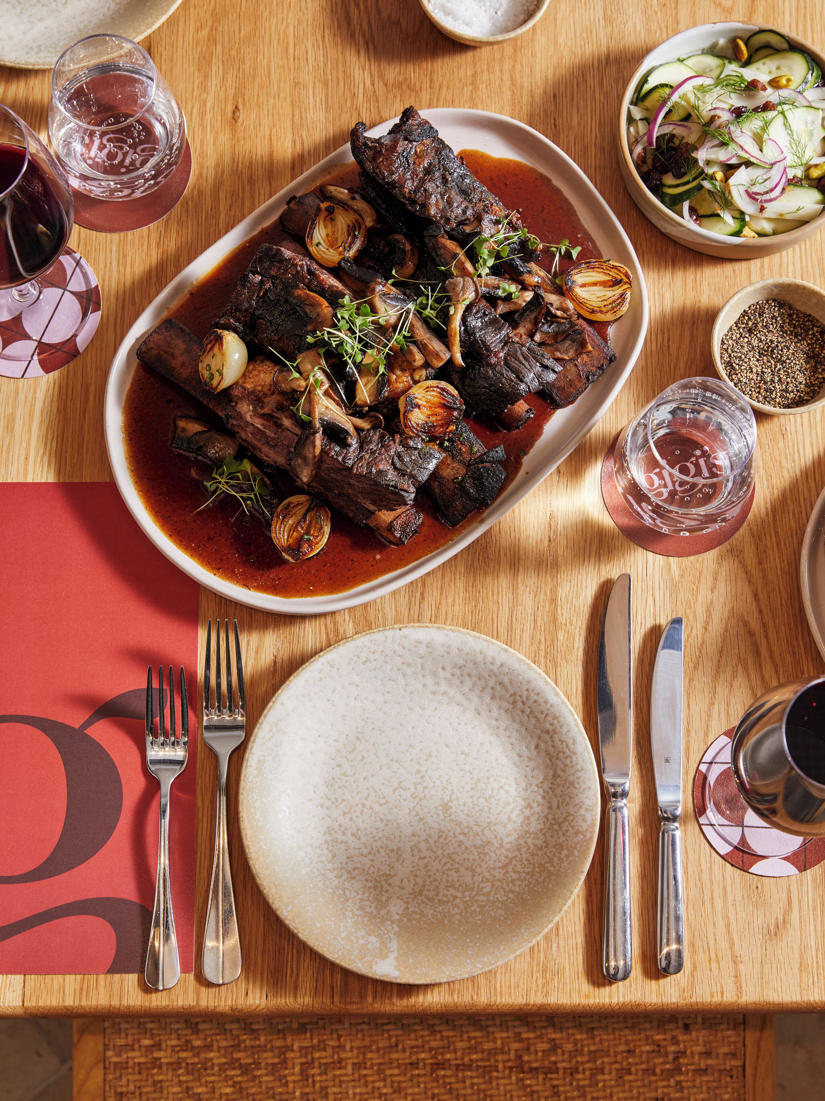 A dining table with a plate of meat, cutlery, and glasses.