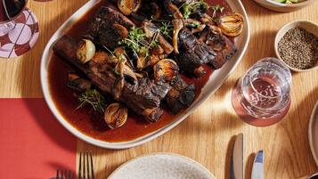 A dining table with a plate of meat, cutlery, and glasses.