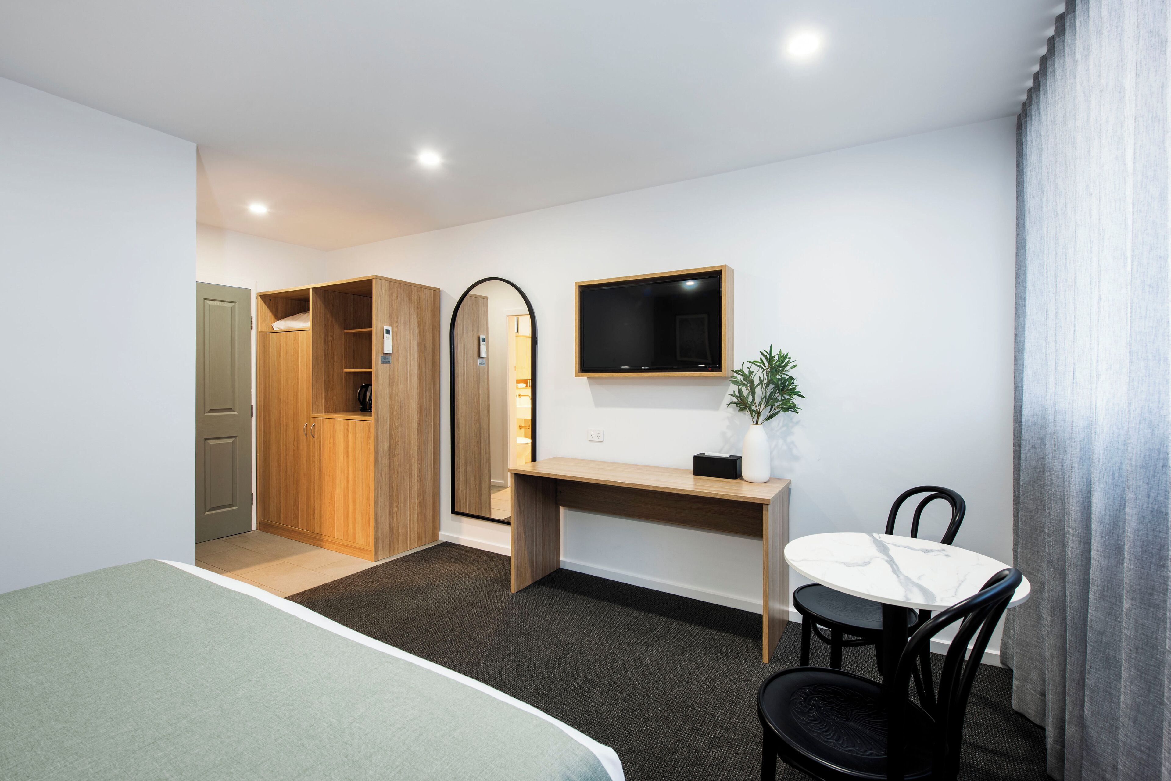 A hotel room with a bed, a desk with a chair, a TV, and a wardrobe.
