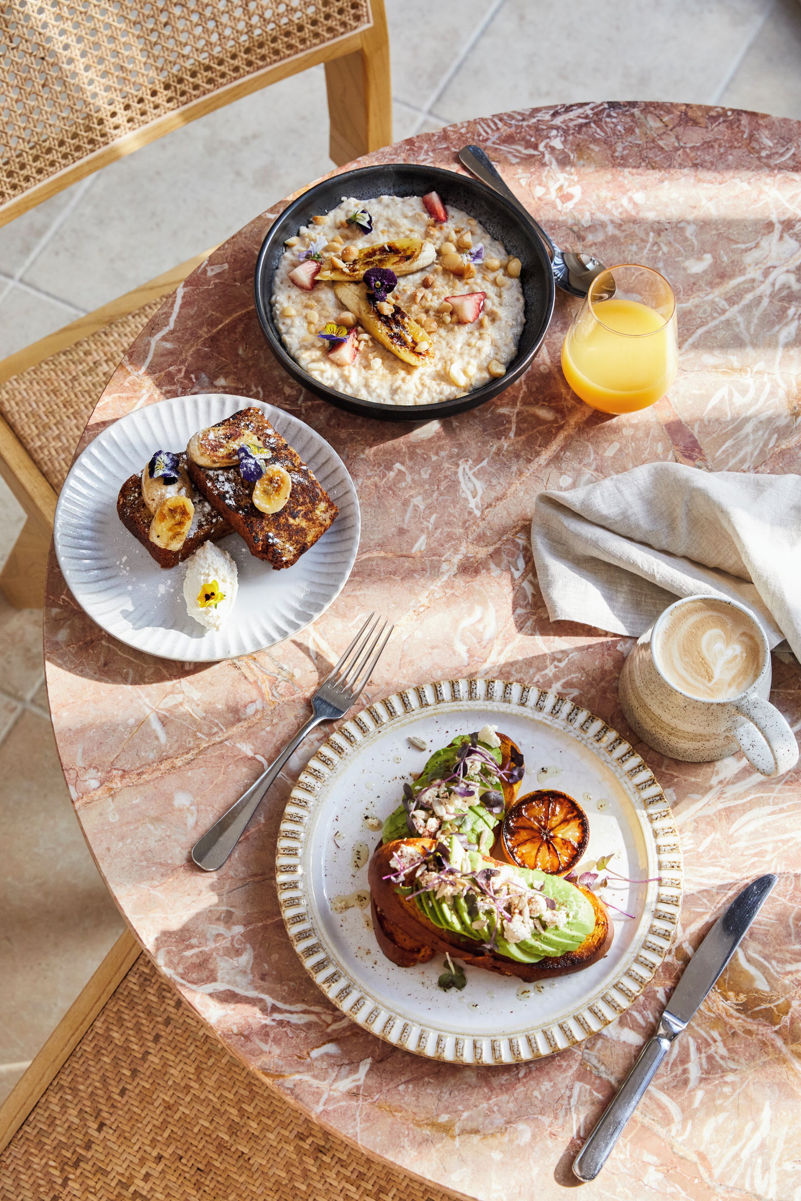 A breakfast table with a bowl of oatmeal, toast with banana slices, a plate with avocado toast, a glass of orange juice, and a cup of coffee.