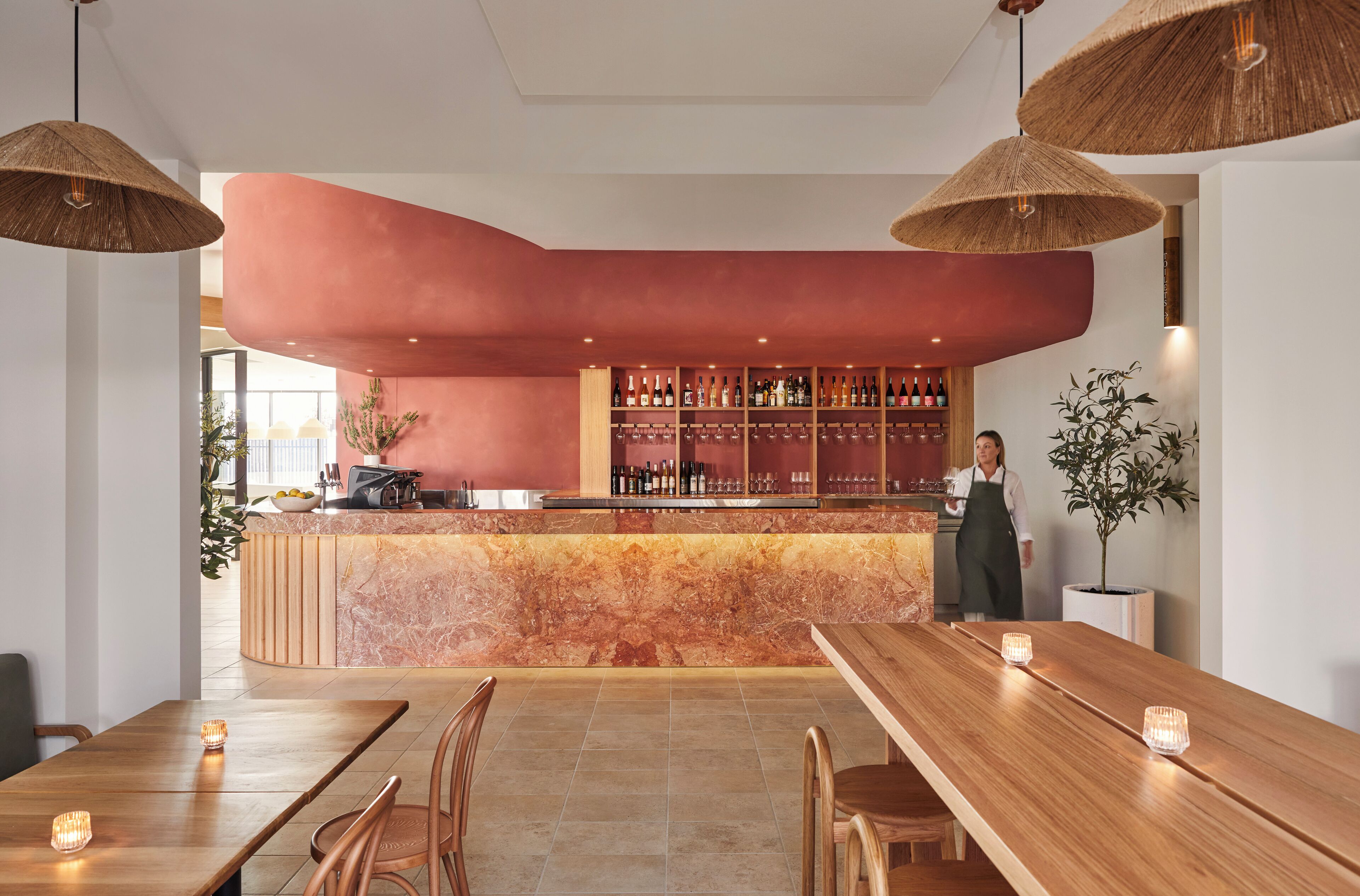 A bar area with a marble counter, wooden tables, and hanging wicker lamps.