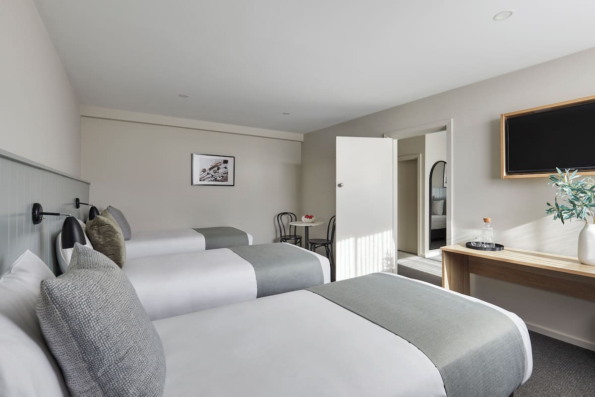 A hotel room with two beds, a desk, a chair, a small table, a plant, and a picture on the wall.