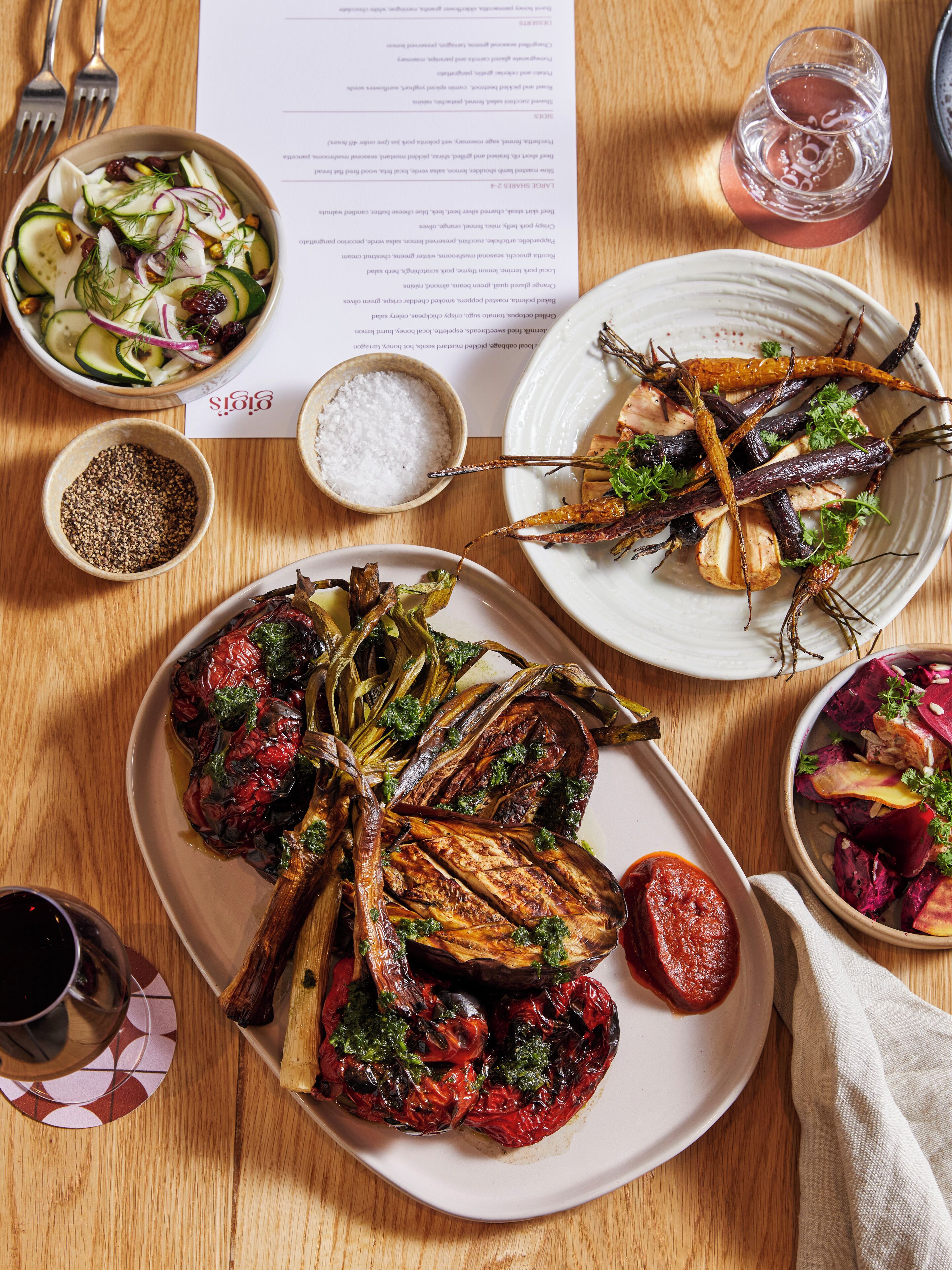 A wooden table with various dishes, including roasted vegetables, a salad, and a plate with a red sauce.