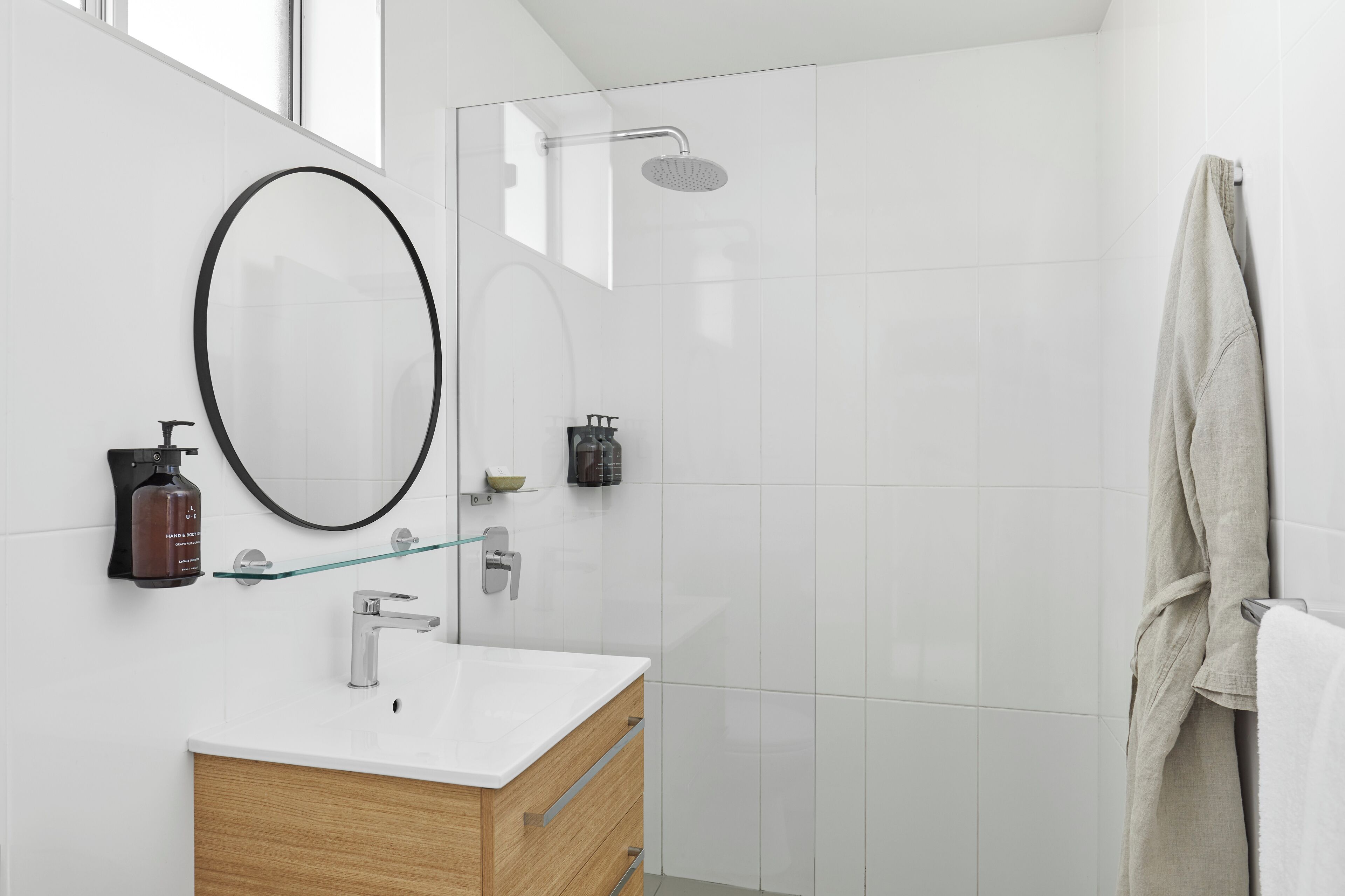 Een moderne badkamer met een douchecabine van glas, een houten wastafelmeubel, een grote spiegel en een handdoekrek.