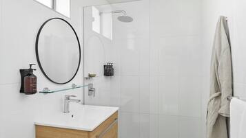 Een moderne badkamer met een douchecabine van glas, een houten wastafelmeubel, een grote spiegel en een handdoekrek.
