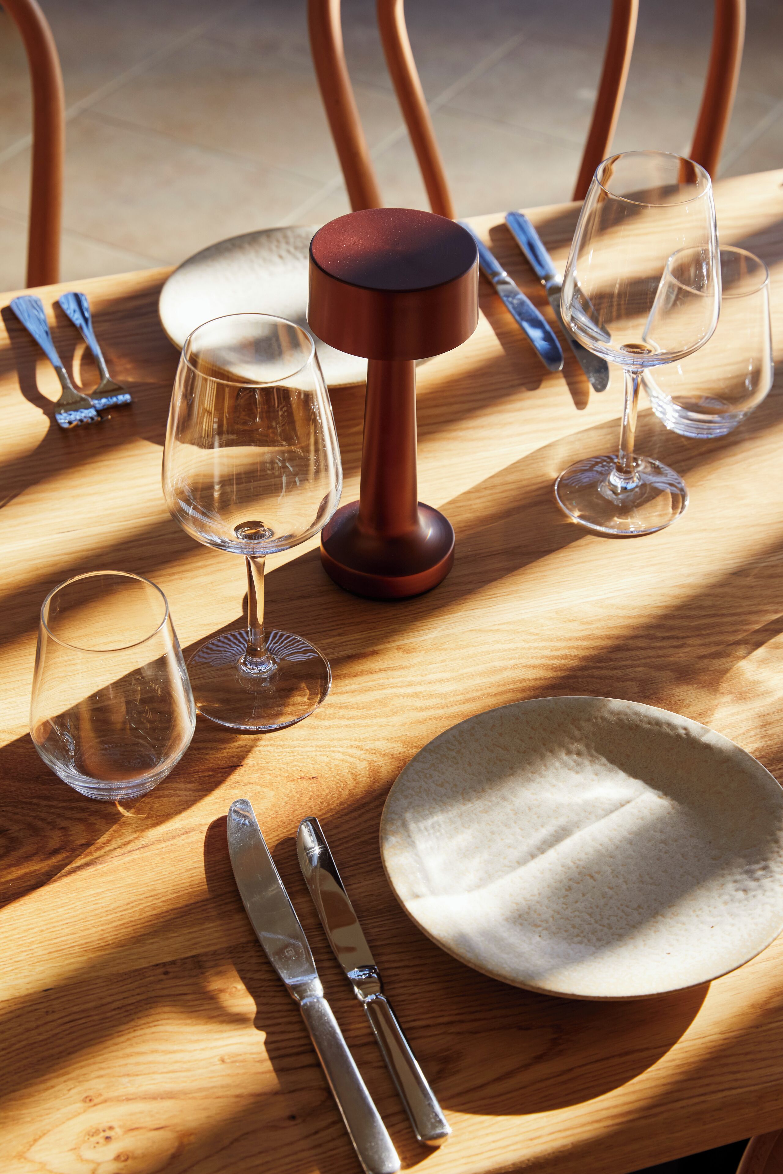 Una mesa de madera con cuatro copas de vino, dos cuchillos y un plato.