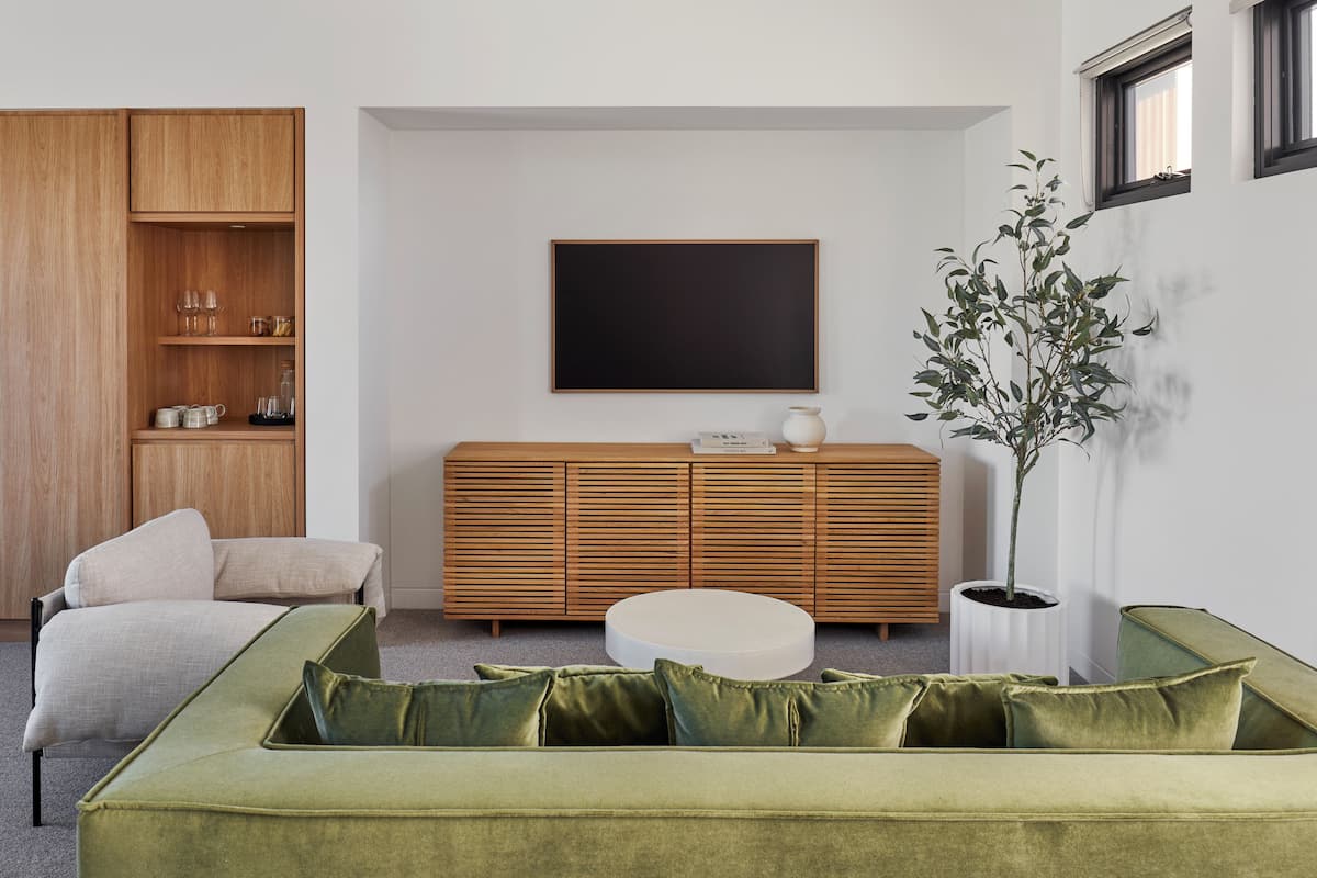 A modern living room with a green sofa, a wooden cabinet, a flat-screen TV, and a potted plant.
