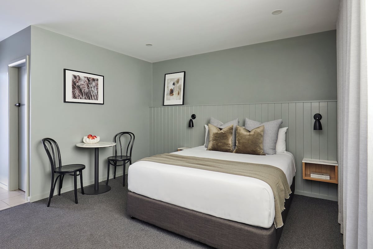 A modern hotel room with a large bed, two chairs, a small table, and two framed pictures on the wall.
