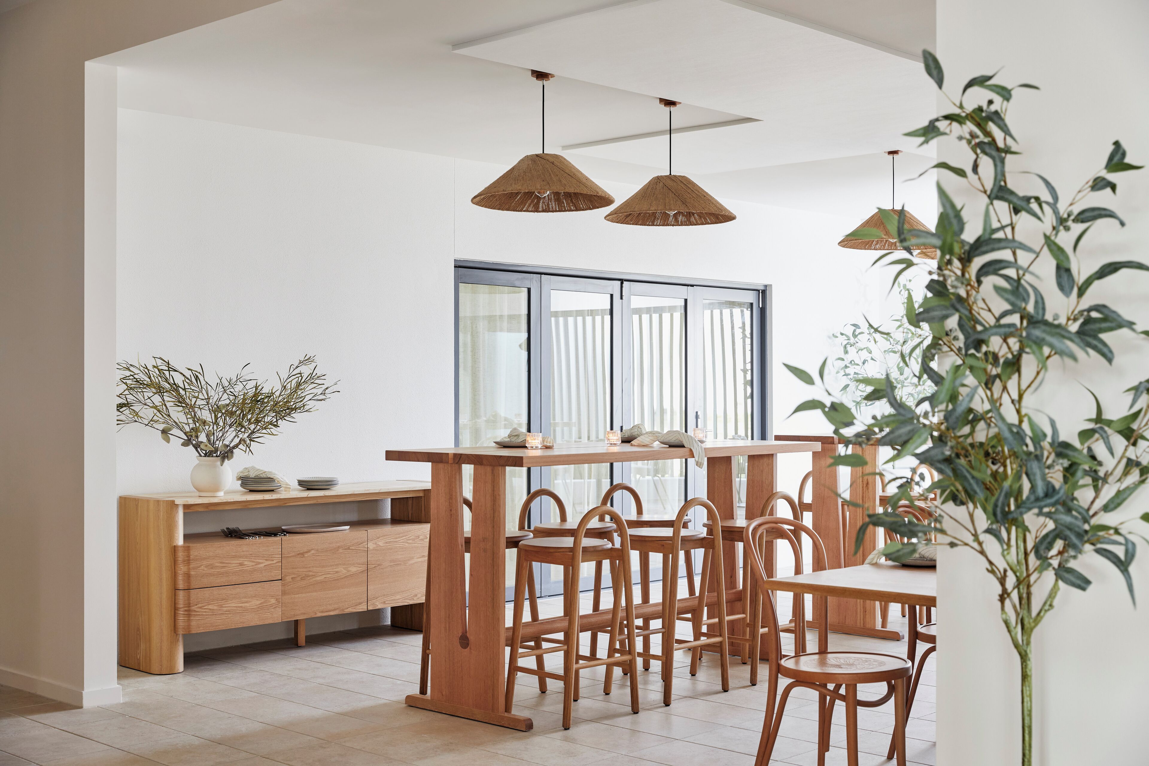 A modern kitchen with wooden furniture, a dining table, and hanging rattan lights.