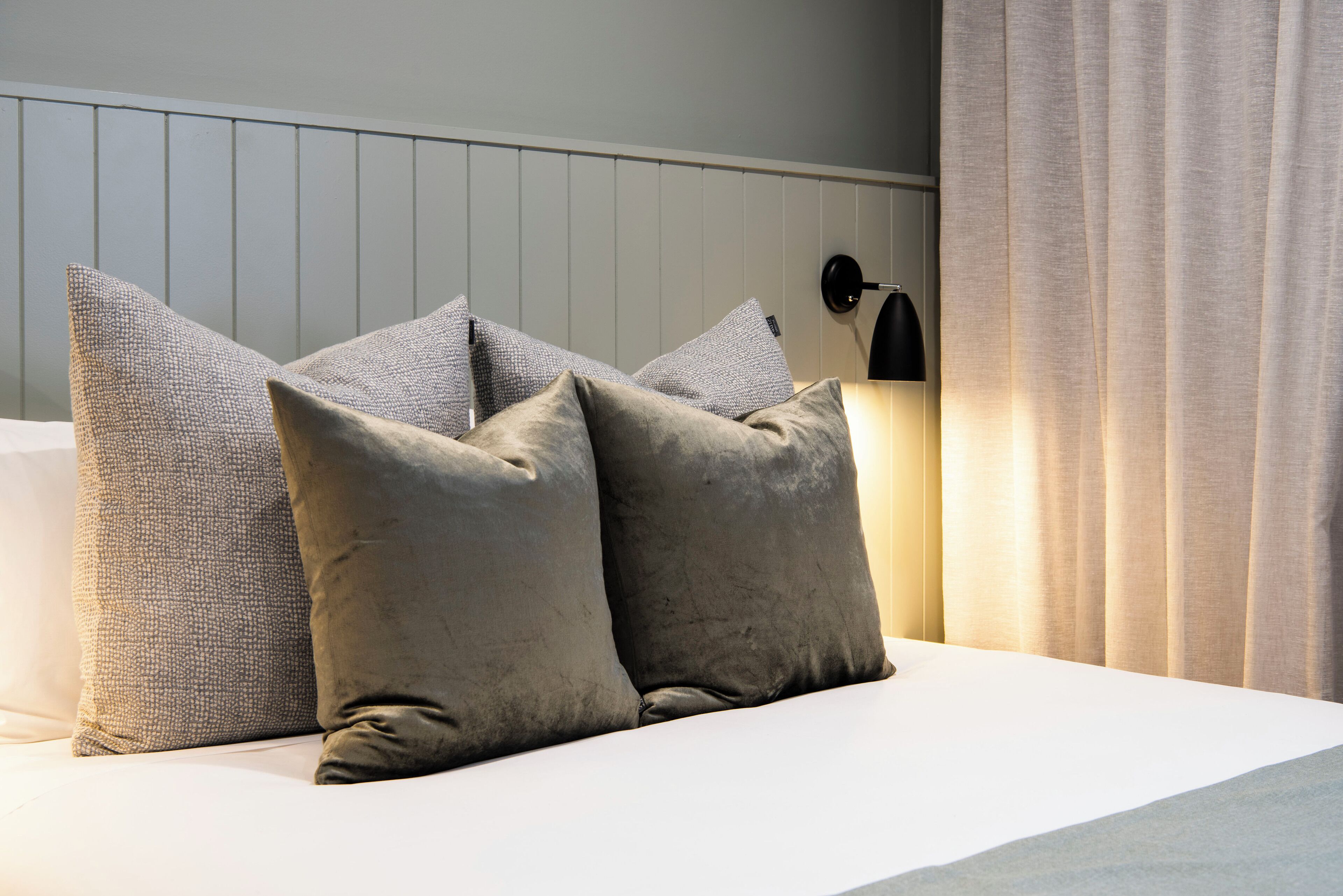 A neatly made bed with a white headboard, two grey pillows, and a black wall-mounted lamp.
