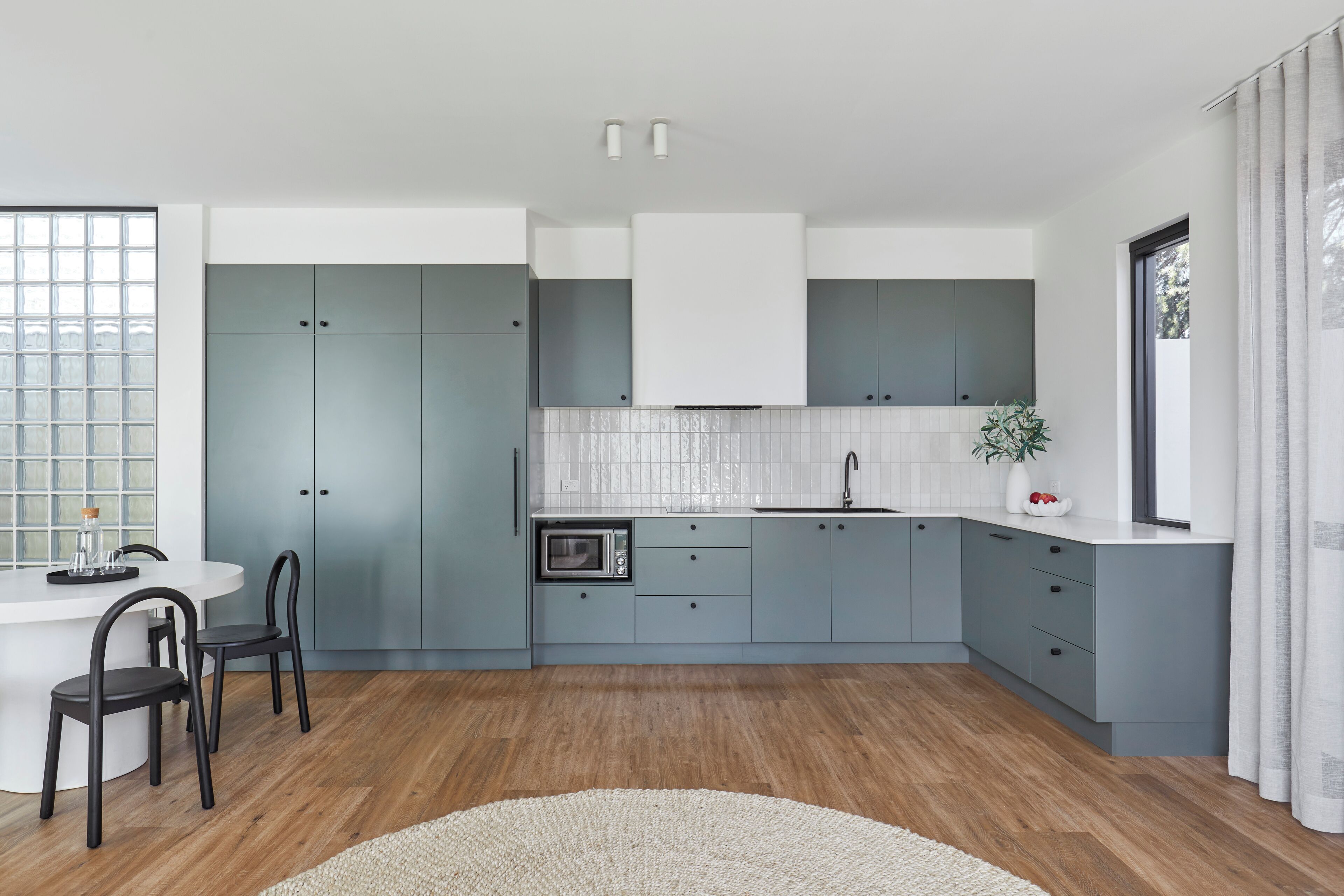 A modern kitchen with grey cabinets, a white countertop, and a wooden floor.
