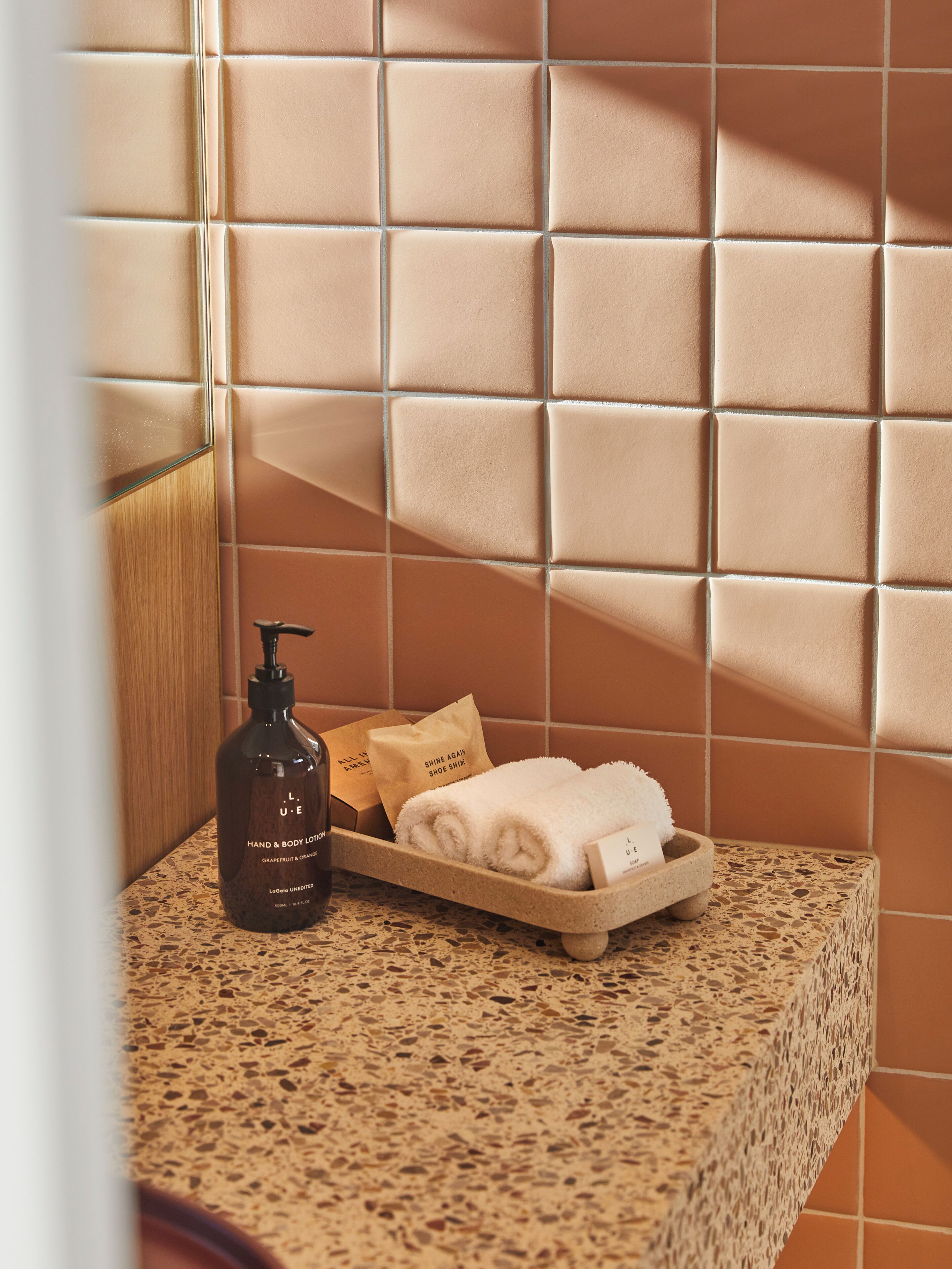 A bathroom with a tiled wall, a soap dispenser, a towel, and a tray with a bag.