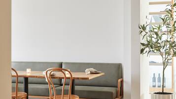 Un comedor con mesa de madera, sillas, un banco con cojín verde y una lámpara colgante.