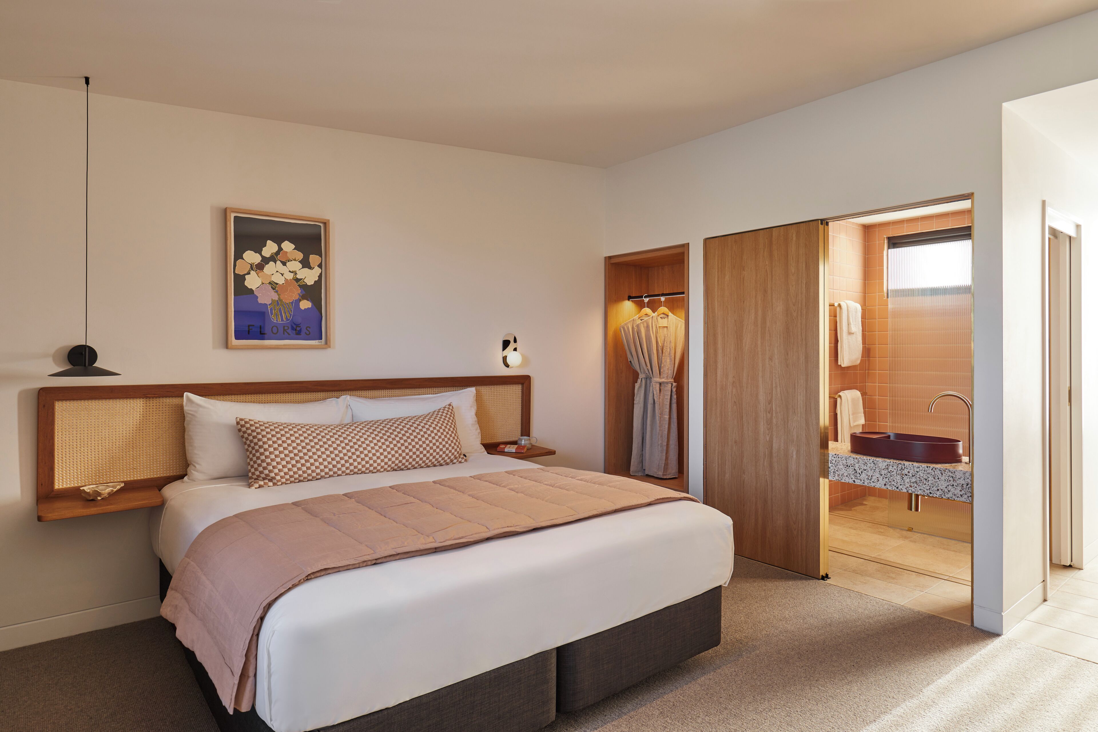 A bedroom with a bed, bedside table, and a bathroom with a sink and mirror.