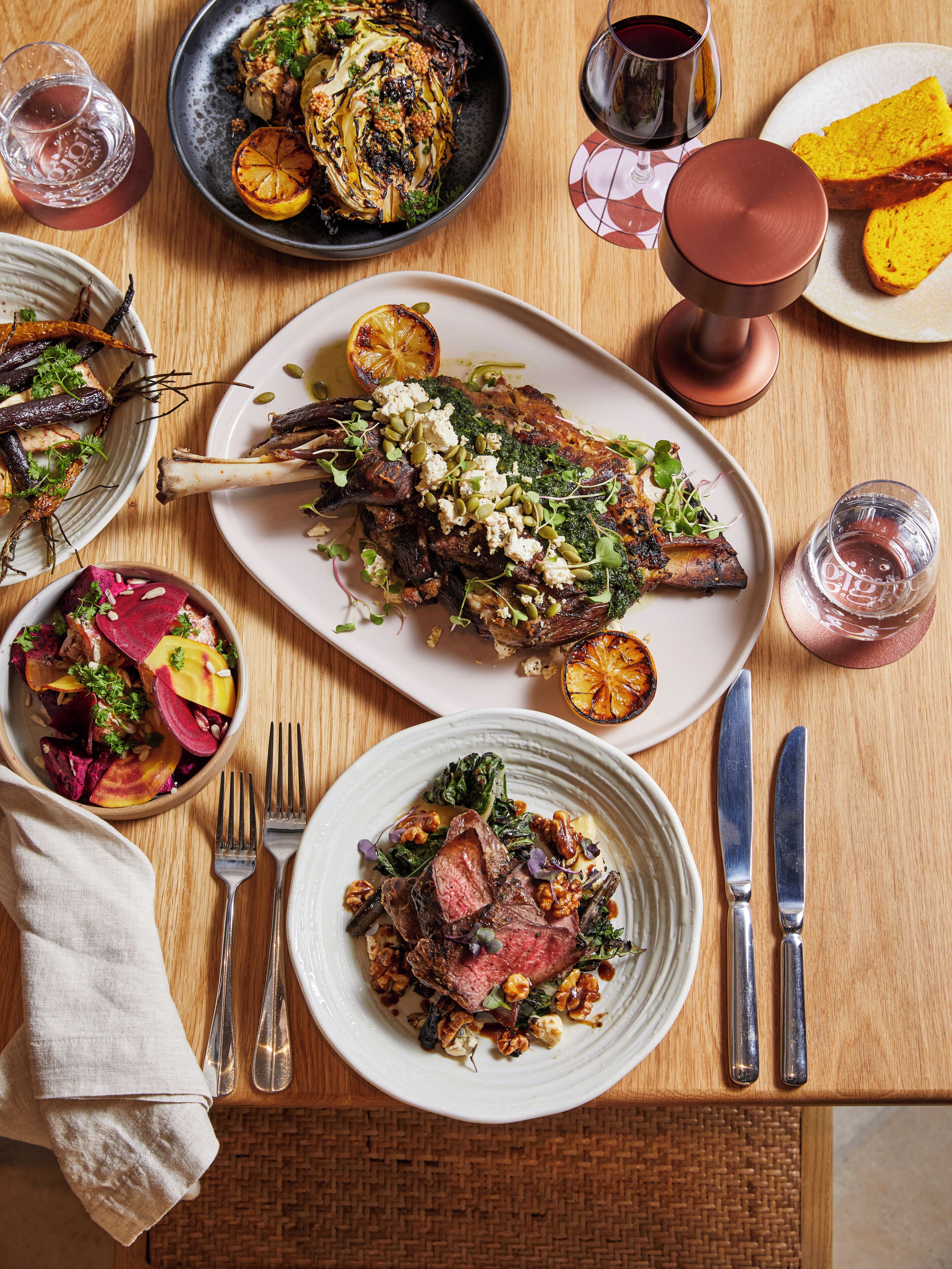 A dining table with various dishes, including a plate of meat, a bowl of salad, and a glass of wine.