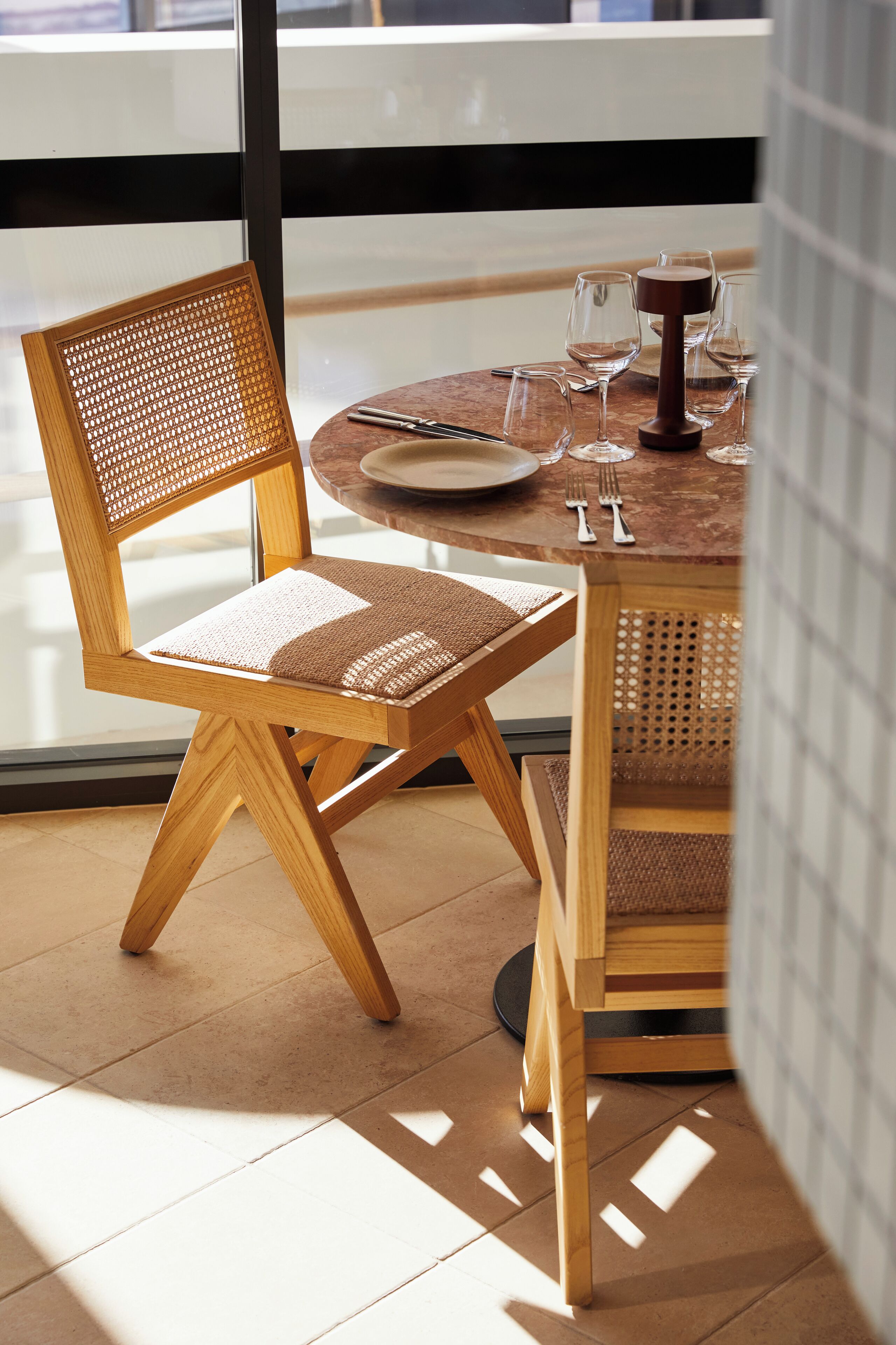 Een houten eettafel met een rieten stoel, een wijnglas en bestek.