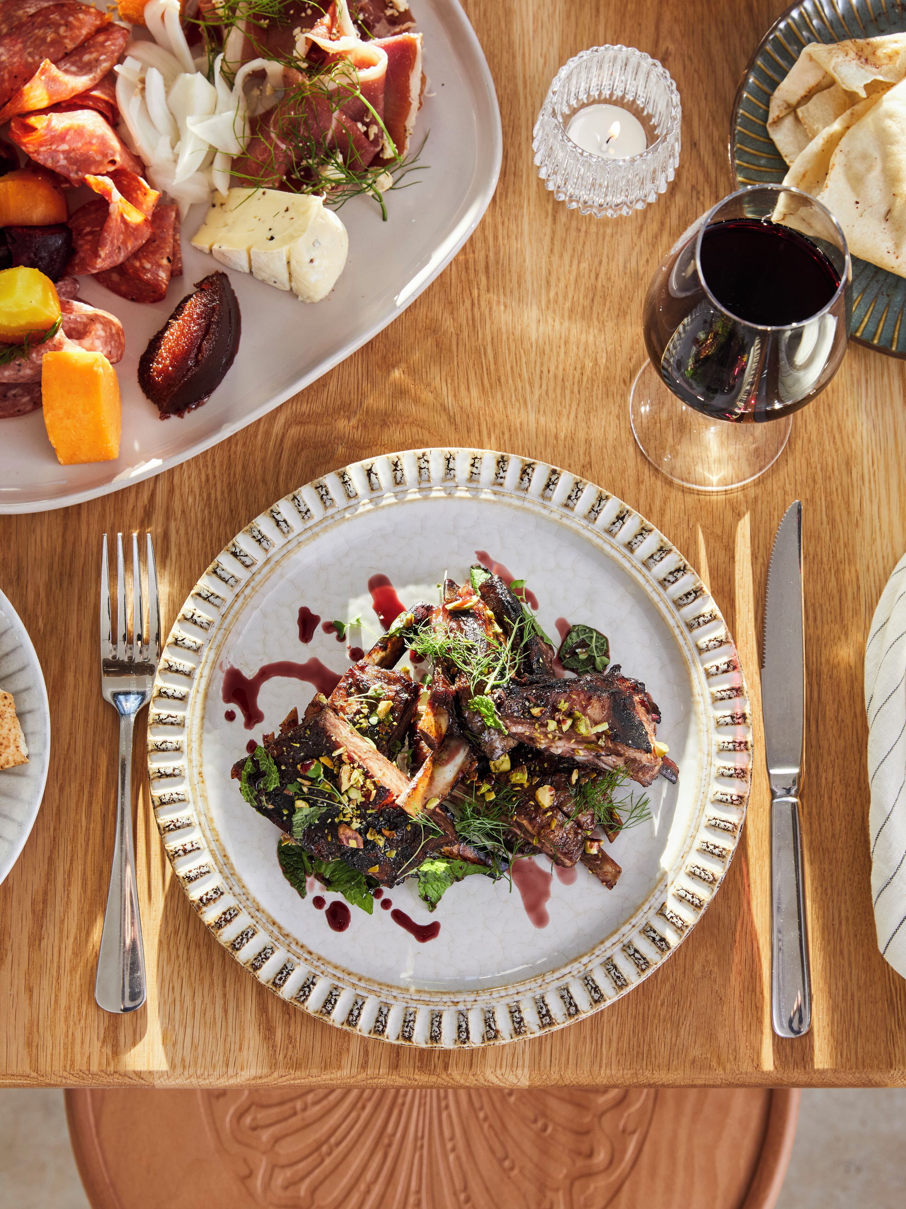 A dining table with plates of food, cutlery, and a glass of red wine.