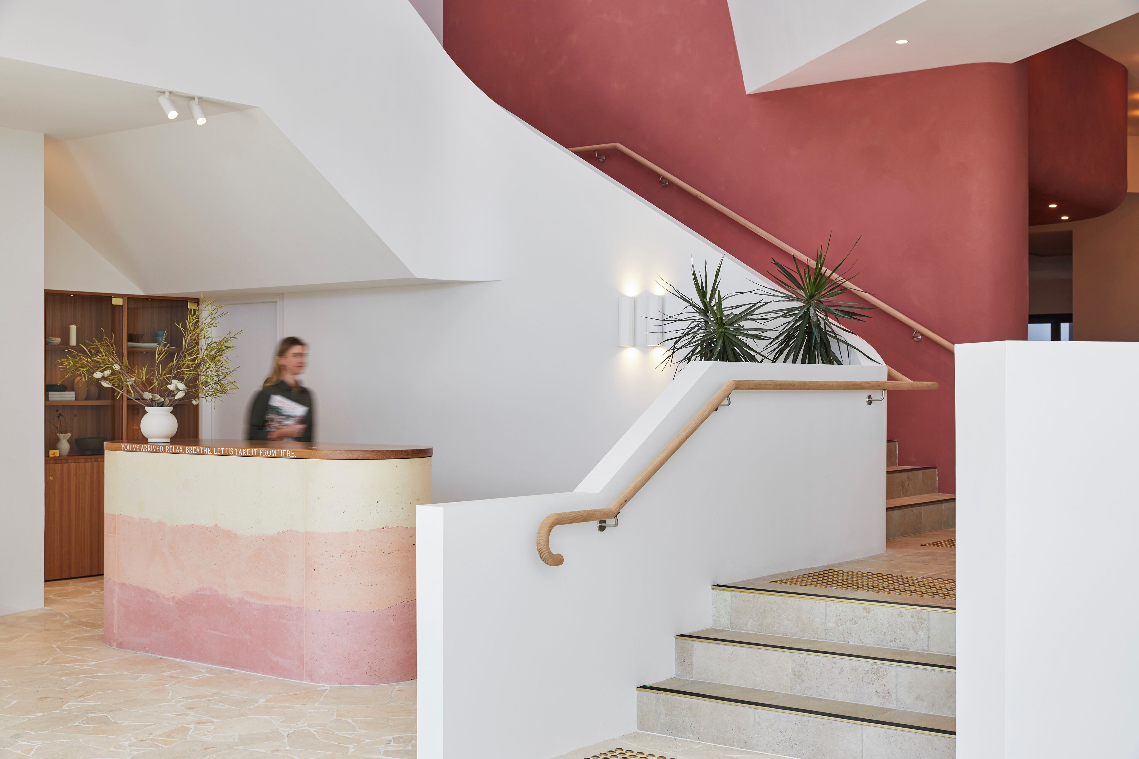 A modern reception desk with a gradient design, a staircase with wooden handrails, and potted plants.