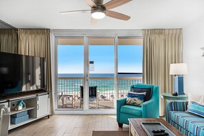 A living room with a large TV, teal armchair, and a sofa with striped cushions. - Pelican Beach Resort 505 (Destin)