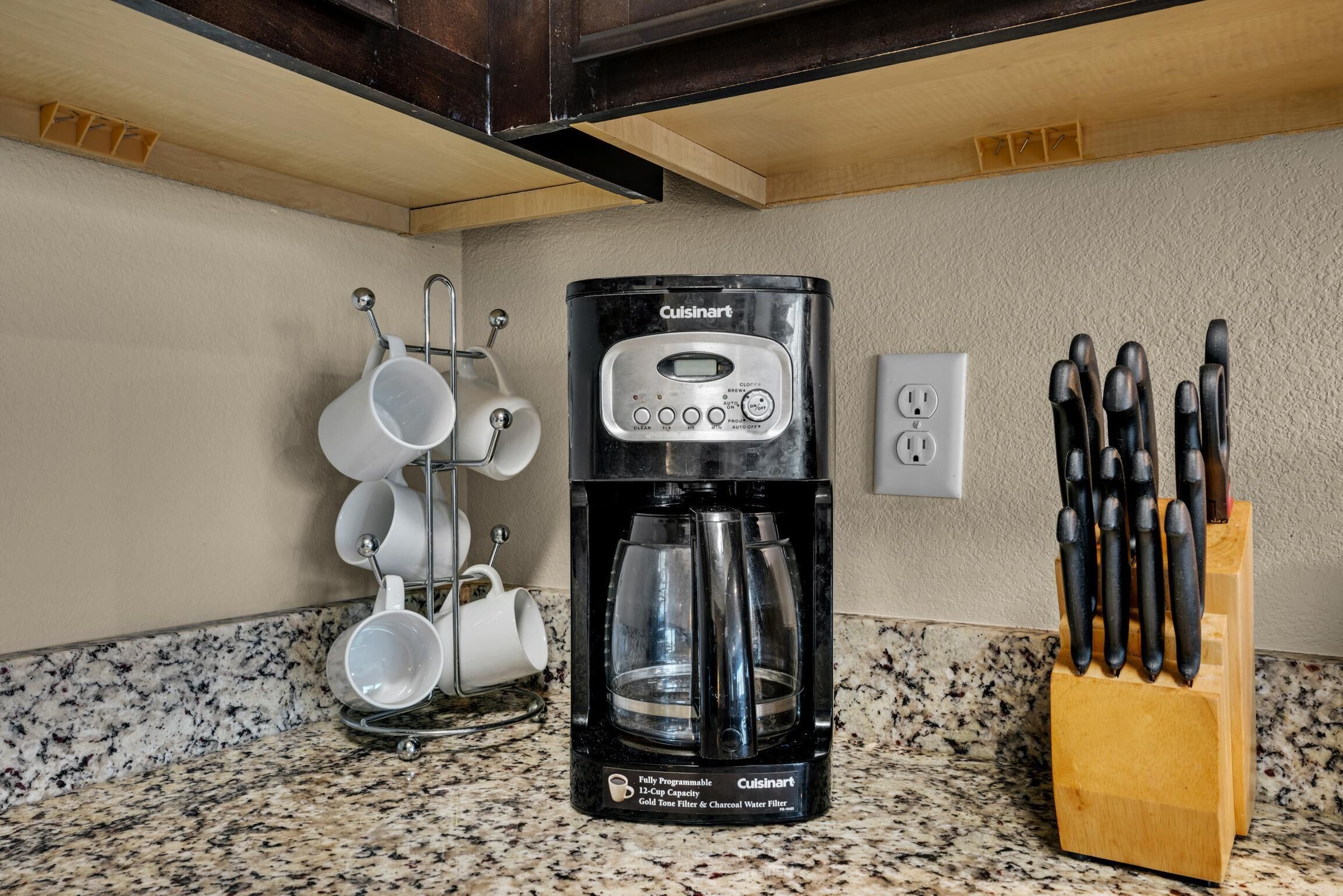 A kitchen with a Cuisinart coffee maker, a mug rack, and a knife block.