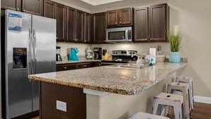 A modern kitchen with dark wood cabinets, stainless steel appliances, and a granite countertop. - Alerio D201 (Miramar Beach)