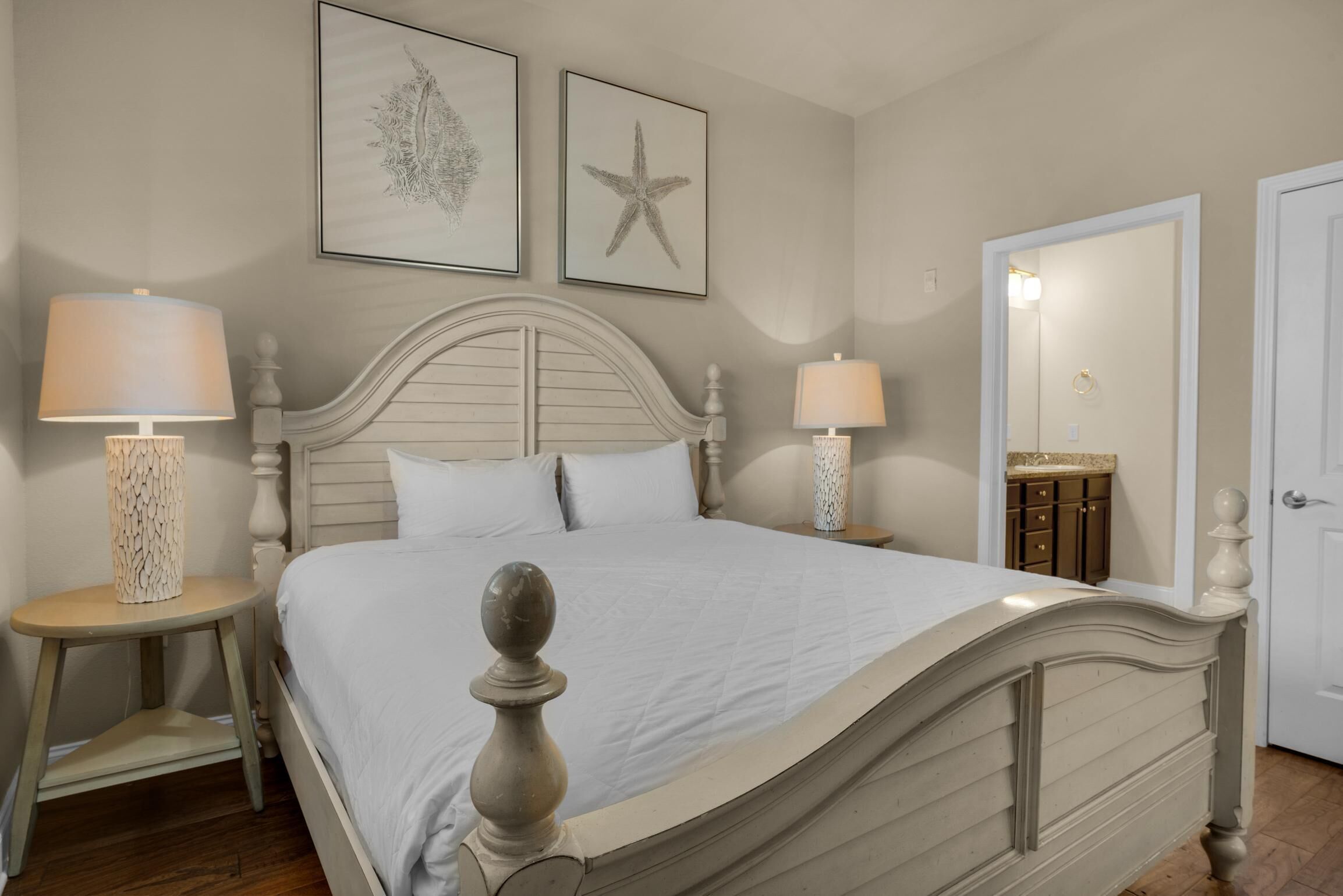 A bedroom with a bed, two bedside tables, a nightstand, a mirror, and artwork on the wall.