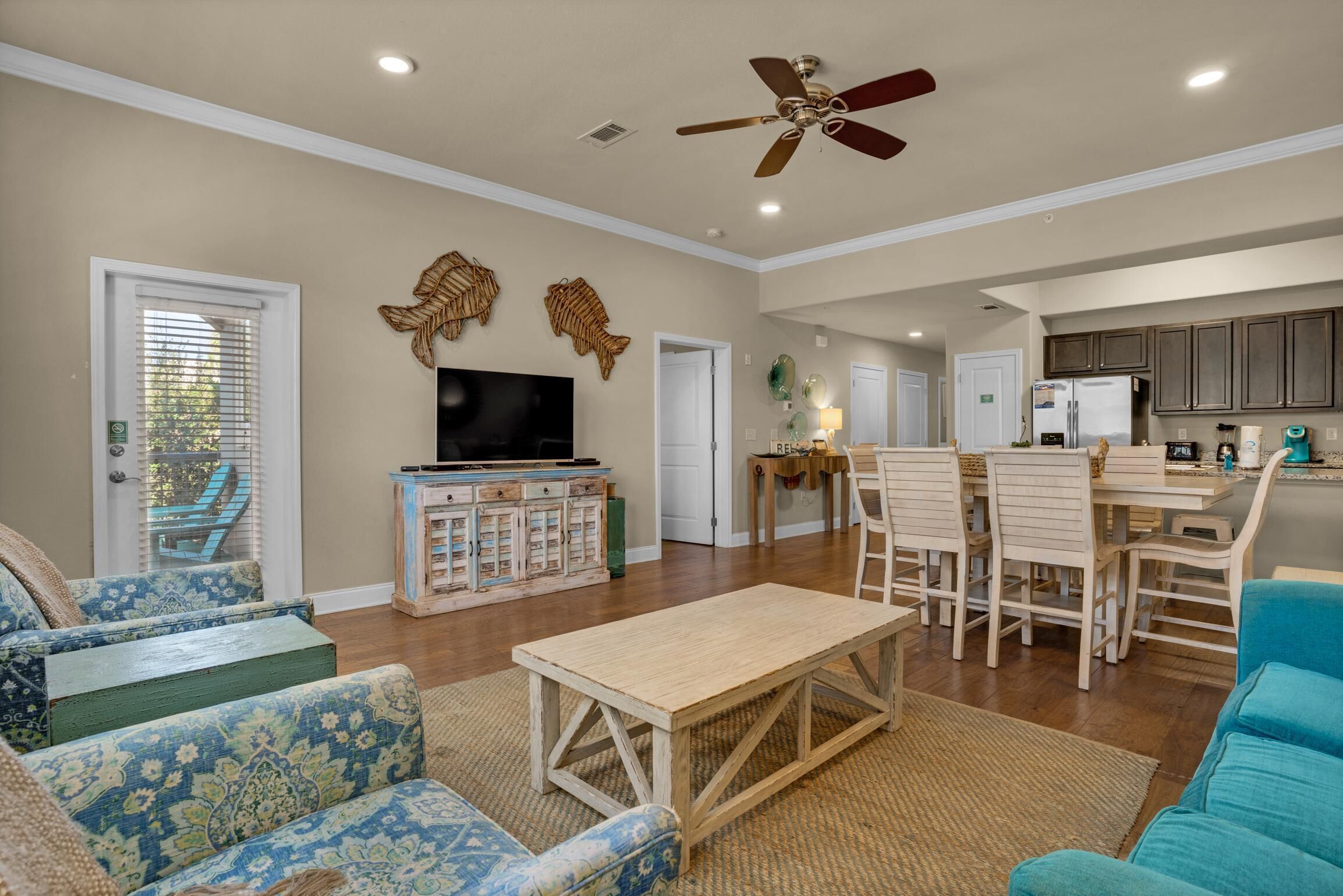 A spacious living room with a television, a dining area with chairs, and a kitchen in the background.