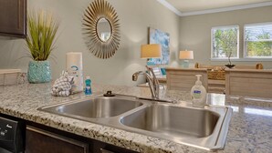 A kitchen with two stainless steel sinks, a marble countertop, a ceiling fan, and a decorative mirror. - Alerio D201 (Miramar Beach)